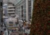 People shopping amidst festive decorations, including a large Christmas tree, inside a Toronto mall.