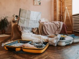 Person packing suitcases with a map in a cozy bedroom, preparing for a journey.