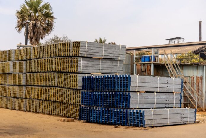 Piles of stacked metal beams in an industrial outdoor yard under a clear sky. Piles of stacked metal beams in an industrial outdoor yard under a clear sky.