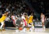 Players in action during an indoor basketball game, with a crowd watching intently.