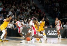 Players in action during an indoor basketball game, with a crowd watching intently.
