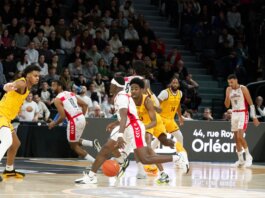 Players in action during an indoor basketball game, with a crowd watching intently.