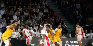 Players in action during an indoor basketball game, with a crowd watching intently.