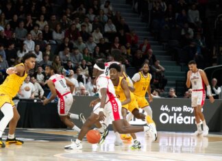 Players in action during an indoor basketball game, with a crowd watching intently.