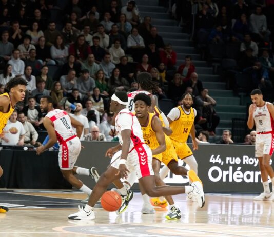 Players in action during an indoor basketball game, with a crowd watching intently.