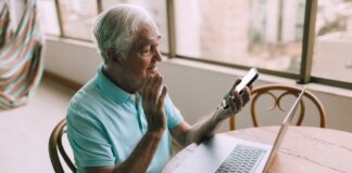 Senior man engaging in a video call using smartphone and laptop indoors.