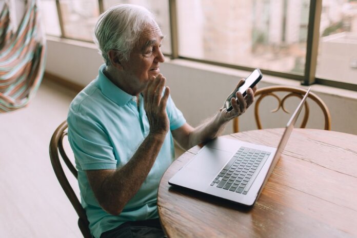 Senior man engaging in a video call using smartphone and laptop indoors. Senior man engaging in a video call using smartphone and laptop indoors.