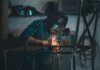 Skilled welder works with sparks in an industrial workshop setting, wearing safety gear.