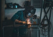 Skilled welder works with sparks in an industrial workshop setting, wearing safety gear.