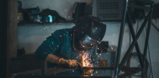 Skilled welder works with sparks in an industrial workshop setting, wearing safety gear.