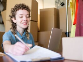 Smiling young woman managing a small business with laptop and packages around her.