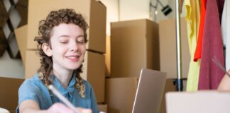 Smiling young woman managing a small business with laptop and packages around her.