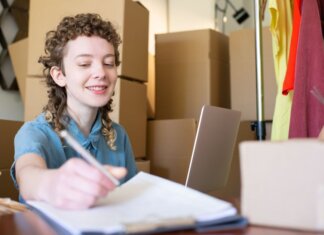 Smiling young woman managing a small business with laptop and packages around her.