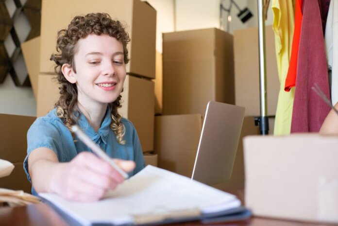 Smiling young woman managing a small business with laptop and packages around her. Smiling young woman managing a small business with laptop and packages around her.