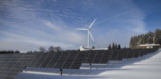 Solar panels and wind turbine in a snowy landscape, showcasing renewable energy sources.