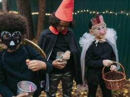 Three children in creative Halloween costumes collect candy outdoors during trick-or-treat.