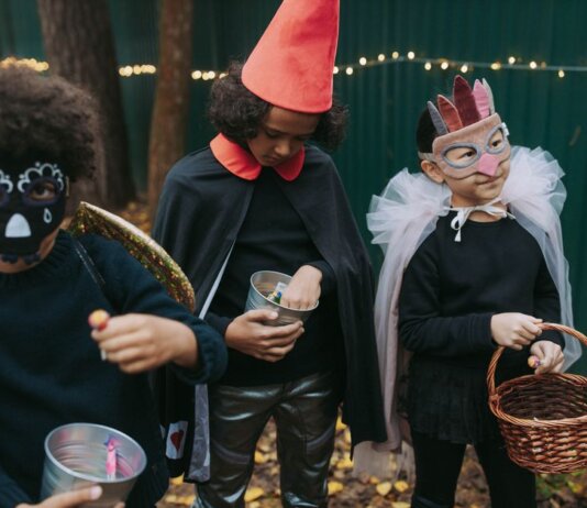 Three children in creative Halloween costumes collect candy outdoors during trick-or-treat.