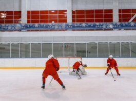 Three hockey players in red uniforms practicing on an indoor ice rink.