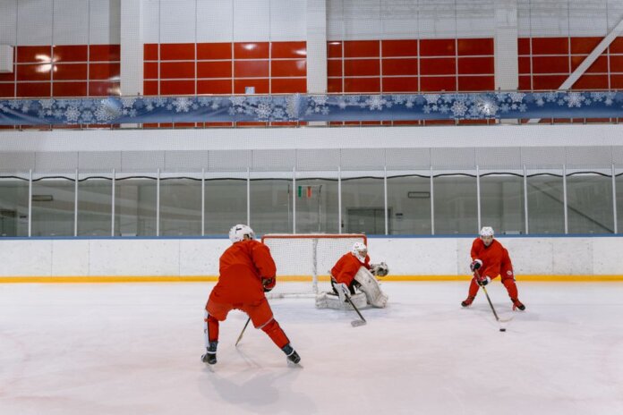 Three hockey players in red uniforms practicing on an indoor ice rink. Three hockey players in red uniforms practicing on an indoor ice rink.