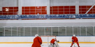 Three hockey players in red uniforms practicing on an indoor ice rink.