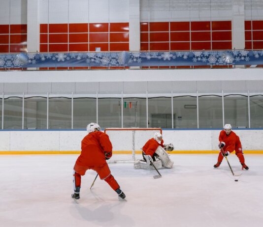 Three hockey players in red uniforms practicing on an indoor ice rink.
