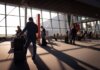 Booking.com: американцы готовы экономить на повседневных тратах ради путешествий Travelers in a bustling airport terminal with carry-on luggage waiting for departure.