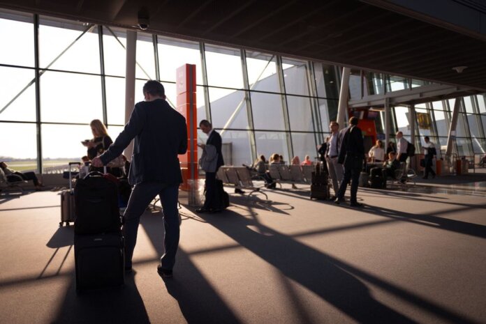 Travelers in a bustling airport terminal with carry-on luggage waiting for departure.