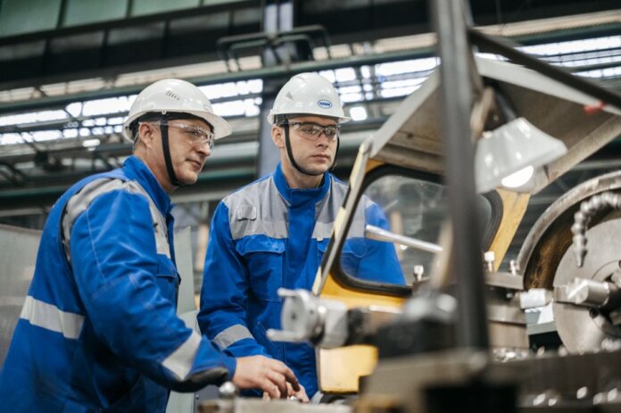 Two industrial workers in protective gear operate machinery in a factory setting. Two industrial workers in protective gear operate machinery in a factory setting.