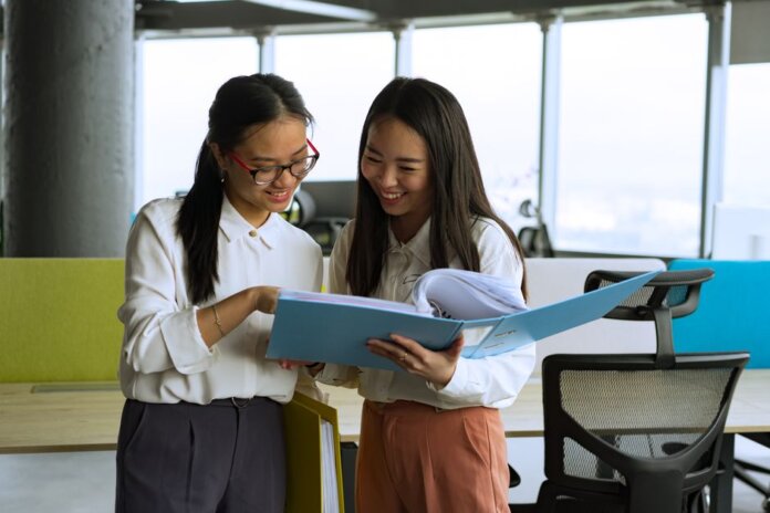 Two young women engaged in a collaborative discussion in a bright, modern office setting. Two young women engaged in a collaborative discussion in a bright, modern office setting.