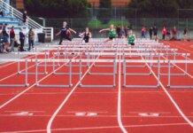 Women athletes compete in a hurdles race at a Victoria track event on a sunny day.