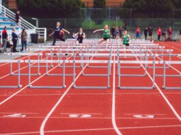 Women athletes compete in a hurdles race at a Victoria track event on a sunny day.