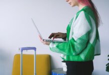 Young woman working on laptop near luggage in stylish hotel lounge, embracing the digital nomad lifestyle.