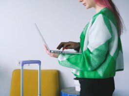 Young woman working on laptop near luggage in stylish hotel lounge, embracing the digital nomad lifestyle.
