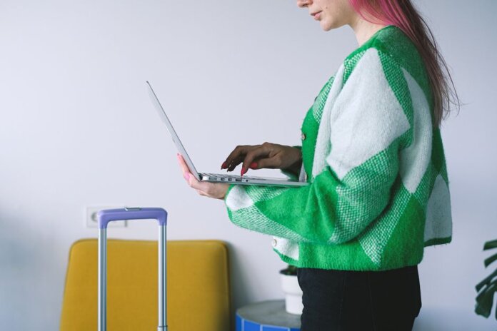 Young woman working on laptop near luggage in stylish hotel lounge, embracing the digital nomad lifestyle.